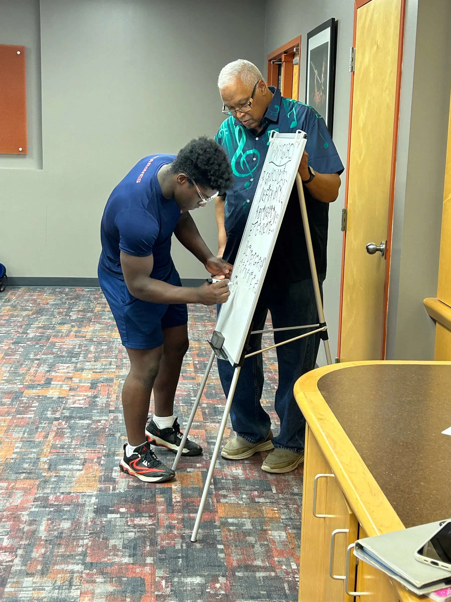 A student writes on a small whiteboard while an instructor holds it steady during class.