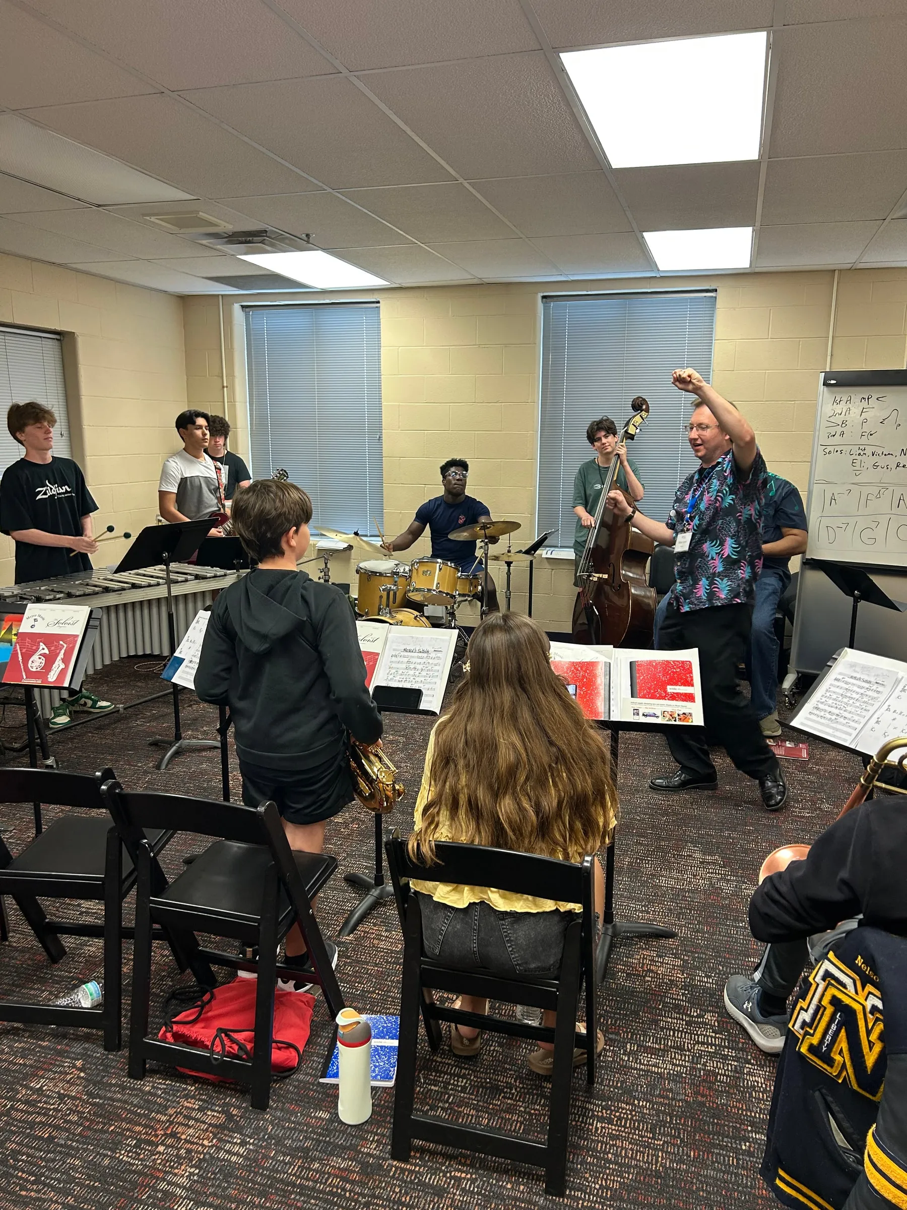 An instructor raises a hand to direct students rehearsing together behind music stands.