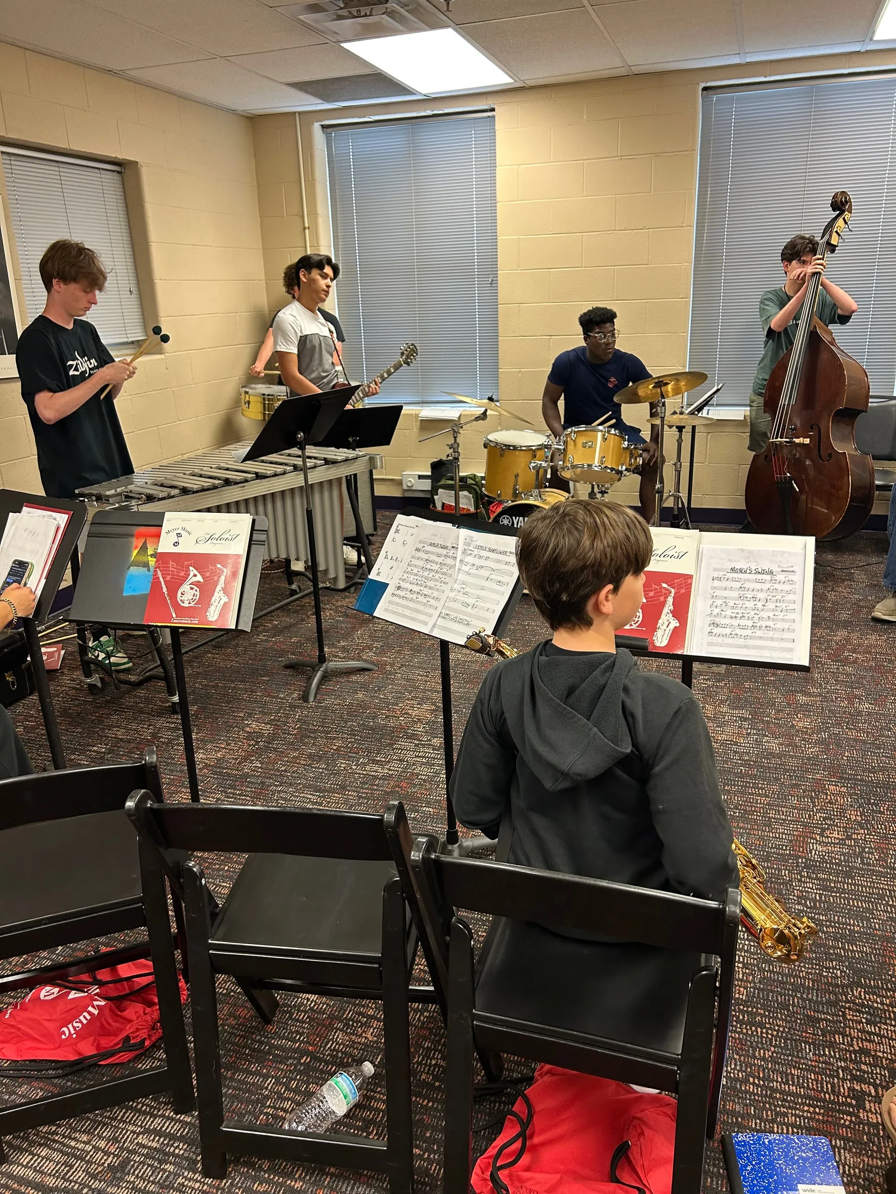 Students rehearse with mallet percussion, drums, and upright bass in a classroom.