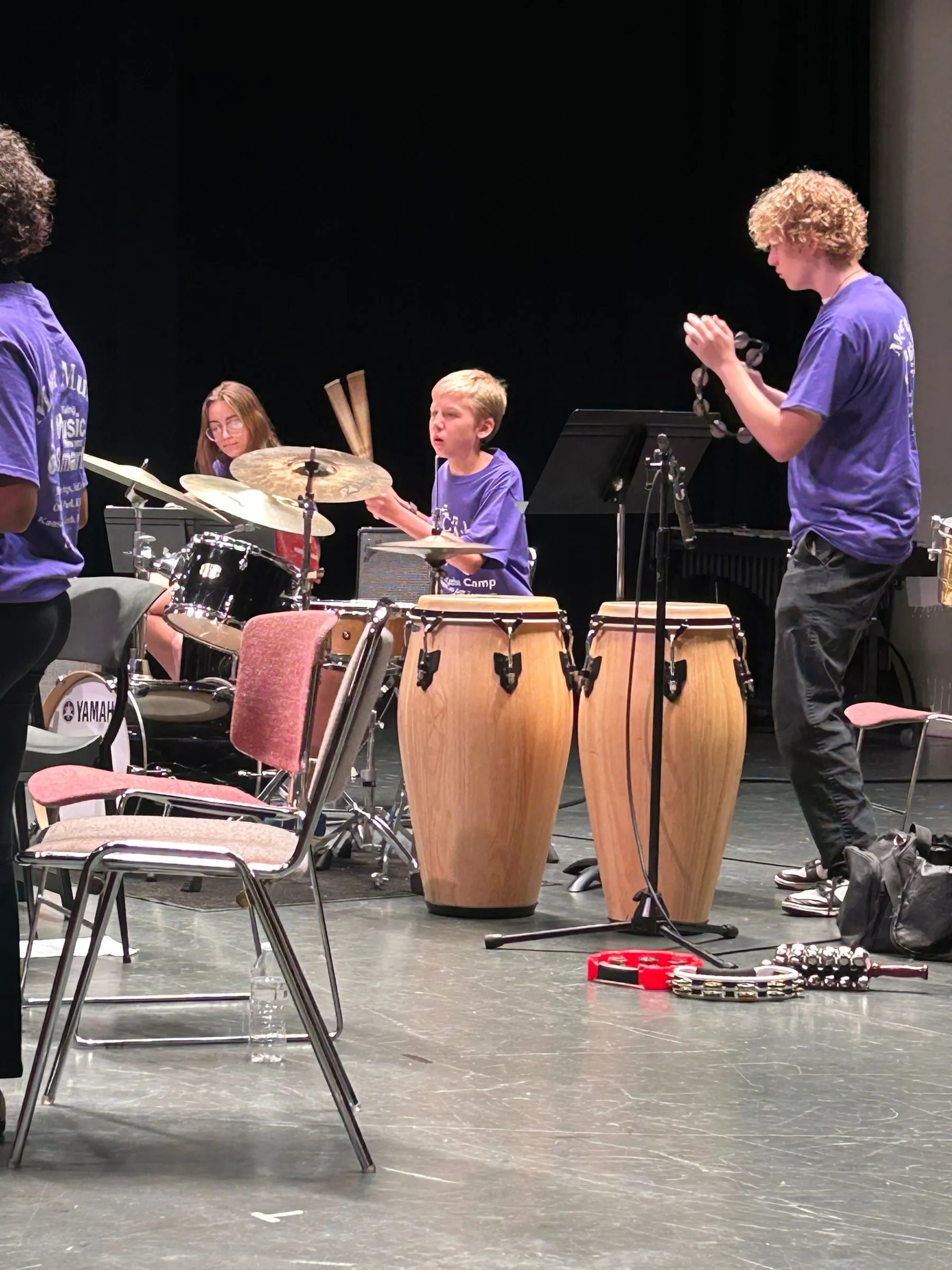 A drummer sits at the drum kit while a fellow camper applauds beside a pair of congas.