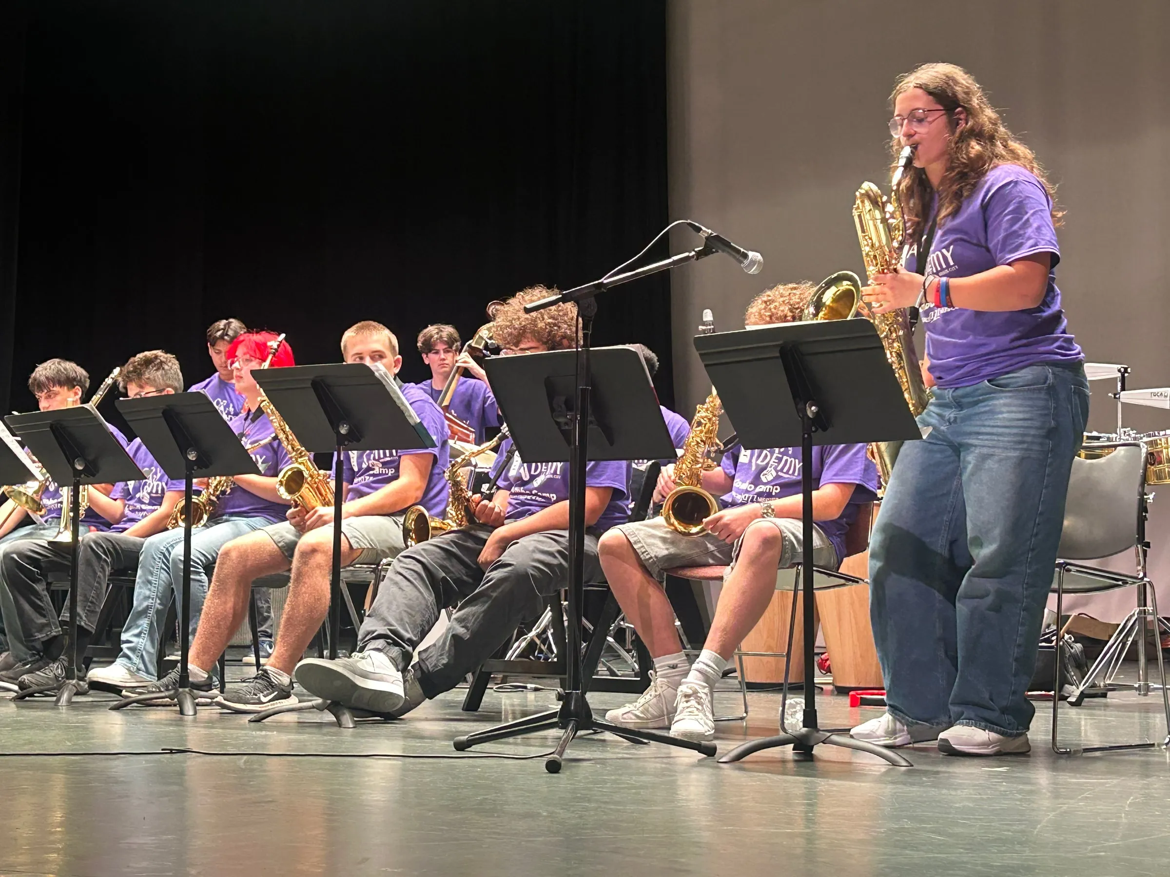 A saxophone soloist stands behind a music stand while other saxophonists sit alongside.