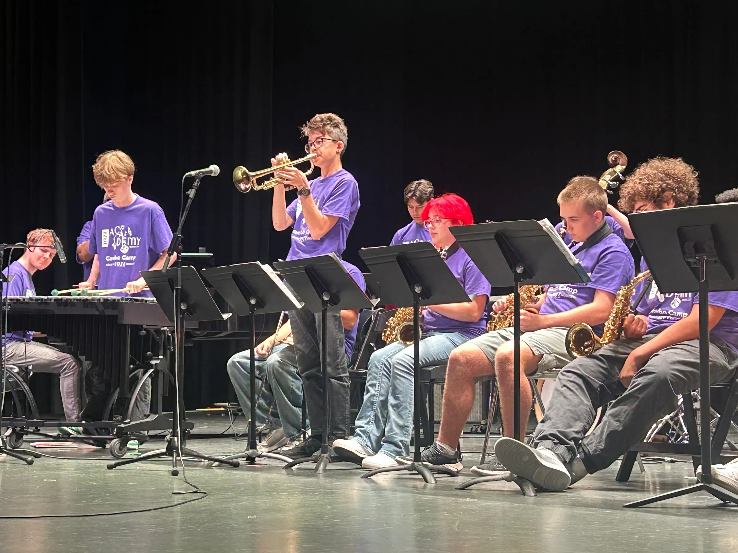 A trumpet soloist stands above the music stands while seated saxophone players follow along.