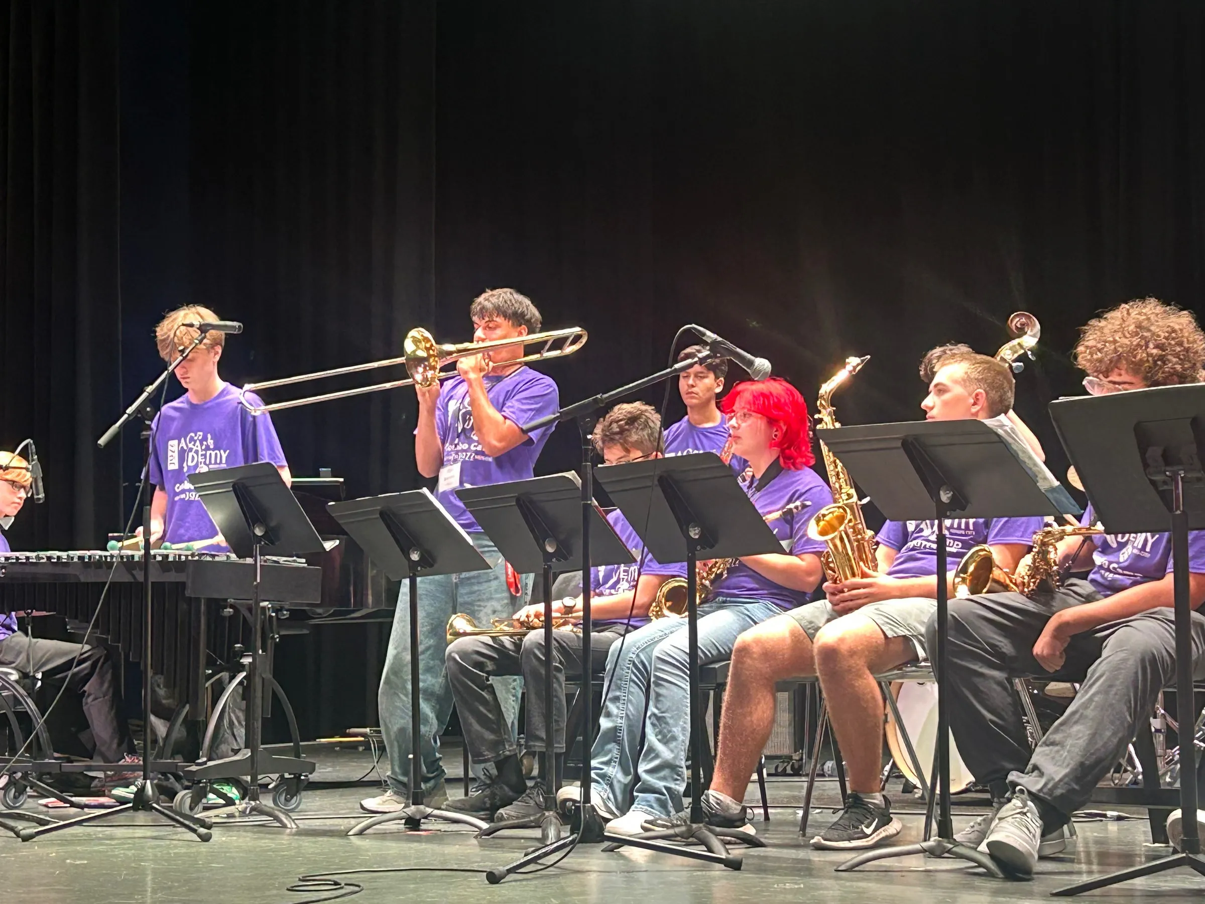 A standing trombonist extends the slide above the seated saxophone section during a solo.