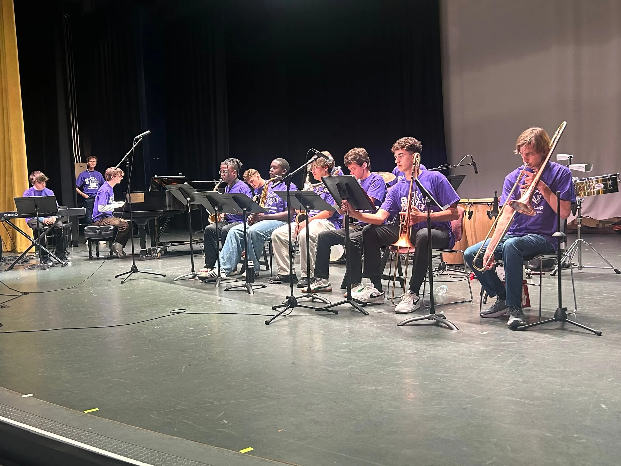 A wide stage view shows a seated jazz ensemble with piano, saxophones, brass, and percussion.