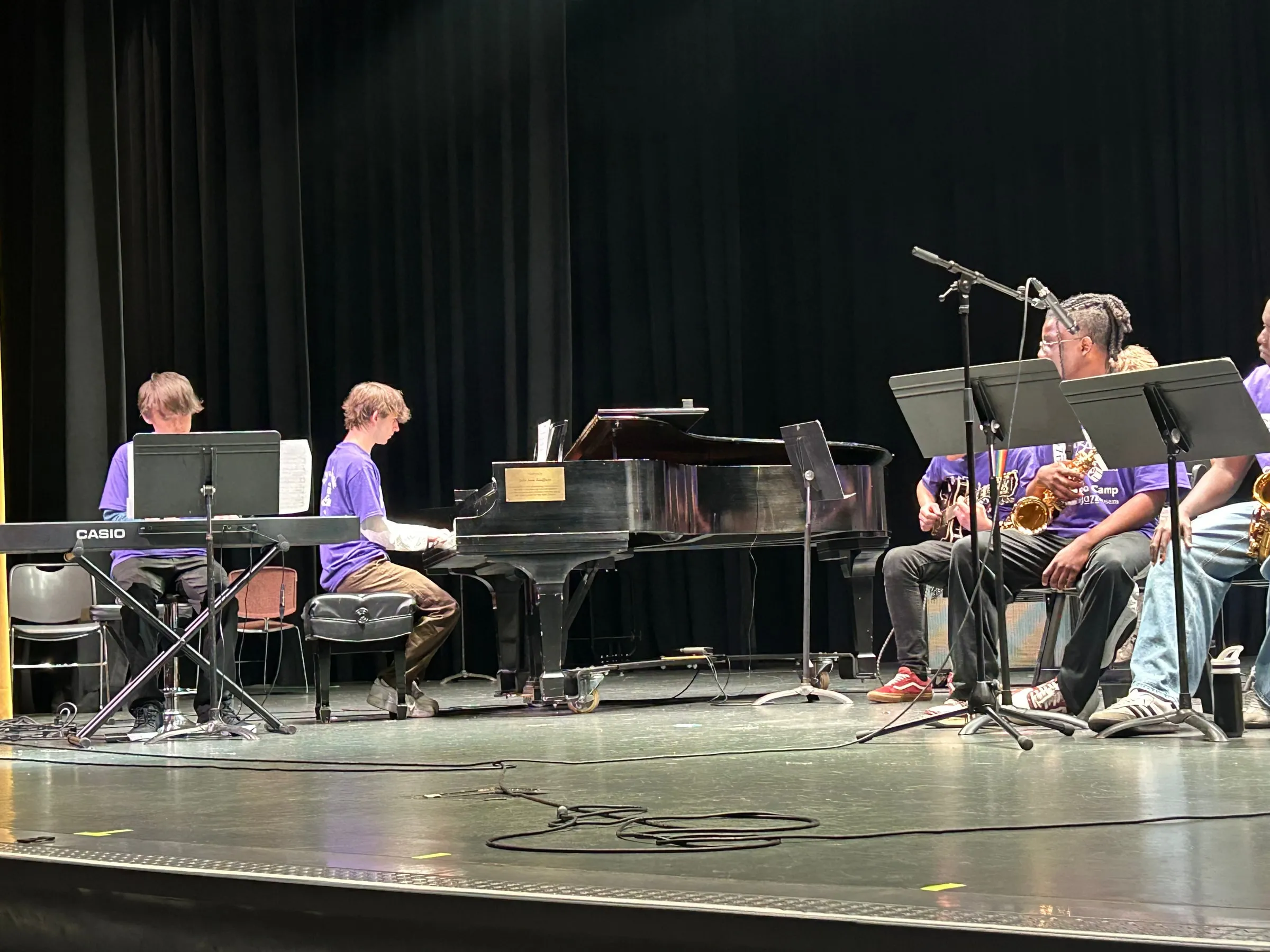 A student plays the grand piano at the side of the stage beside a keyboard and the seated horn section.