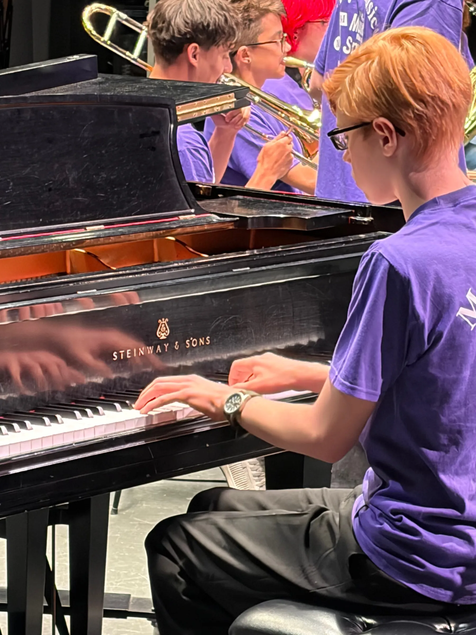 A close view of a student pianist's hands on the keys, reflected in the polished side of the grand piano.