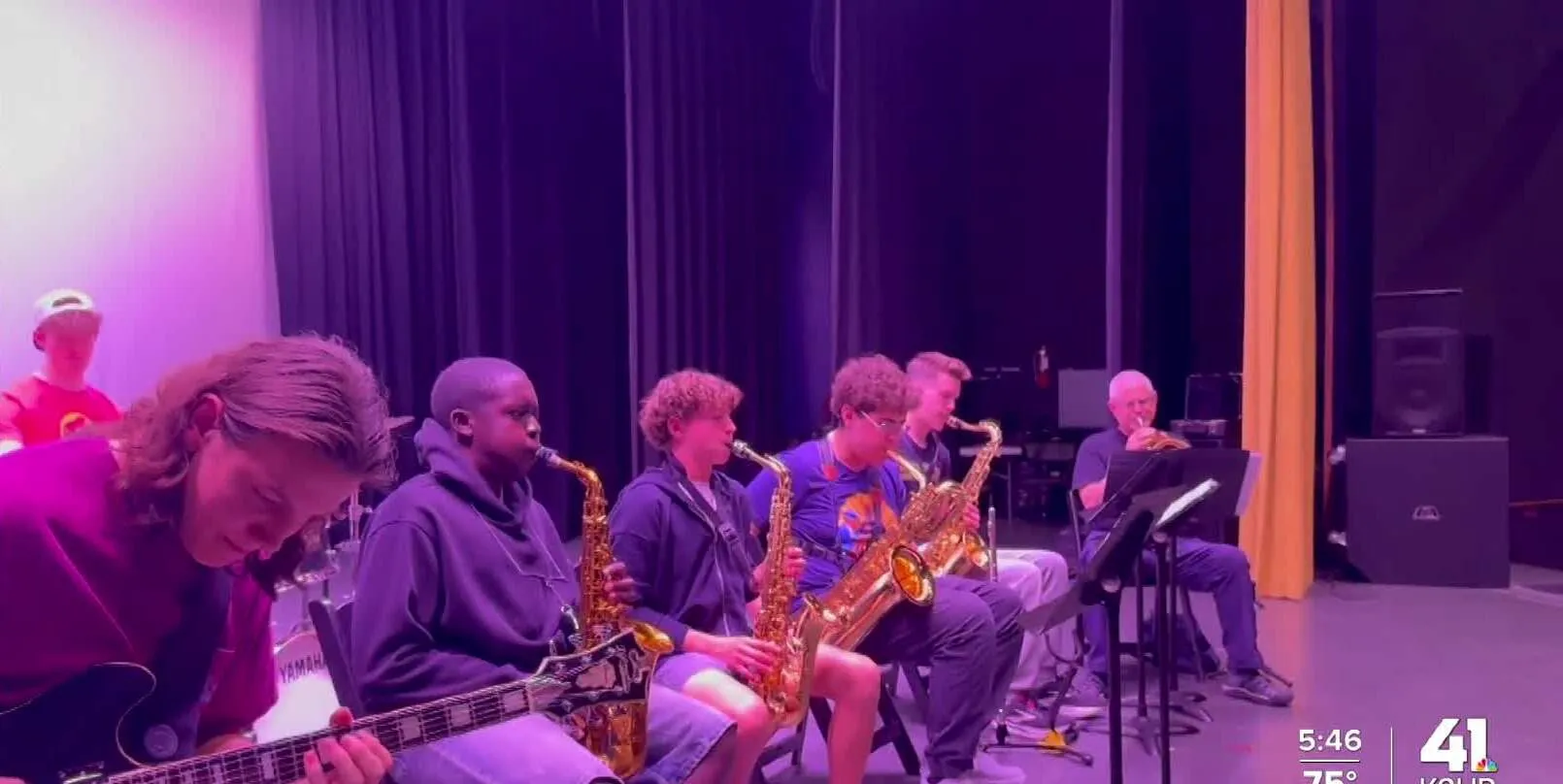 Kansas City Jazz Academy students play electric bass and saxophones on stage under stage lighting, in a still from a KSHB 41 news feature.